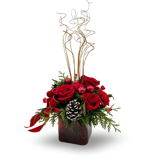 Christmas floral arrangement with red roses, glittery branches, pinecones, and holiday greenery in a square red glass cube.